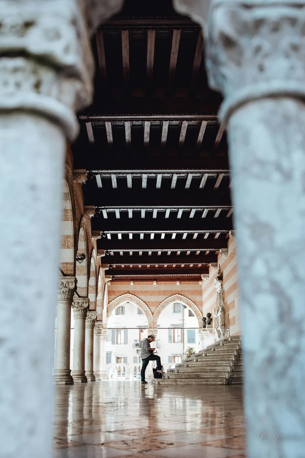 Il porticato della Loggia del Lionello a Udine visto tra due colonne, con il soffitto a travi e un fotografo sui gradini
